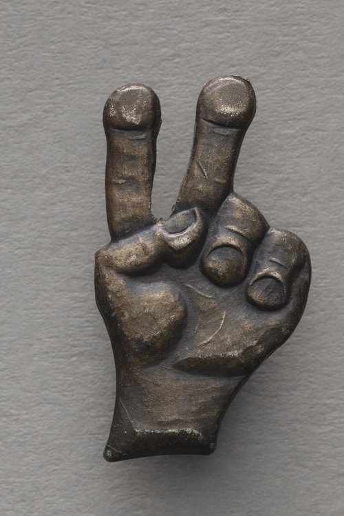 Przypinka w kształcie dłoni z palacmi ułożonymi w literę V