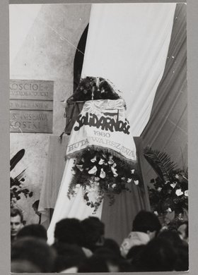 Pogrzeb bł. ks. Jerzego Popiełuszki - katafalk ze zwłokami kapłana otoczony chorągwiami, wieńcami i wiązankami kwiatów
