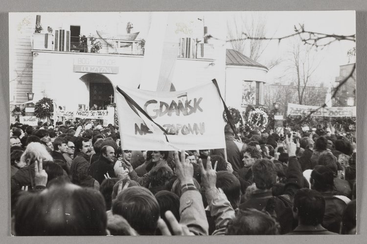 Pogrzeb bł. ks. Jerzego Popiełuszki - ludzie na tle kościoła p.w. św. Stanisława Kostki na warszawskim Żoliborzu trzymający transparenty oraz wyciągnięte w górę prawe ręce