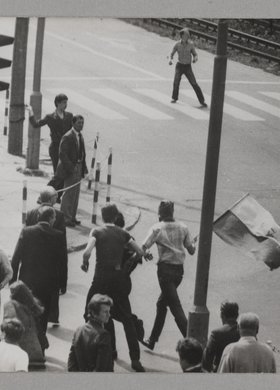 Zamieszki na ulicach miasta - ludzie z flagami biegnący i rzucający kamieniami