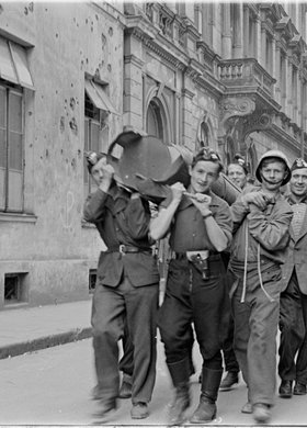 Powstańcy niosący zasobnik zrzutowy na ulicy Wojciecha Górskiego