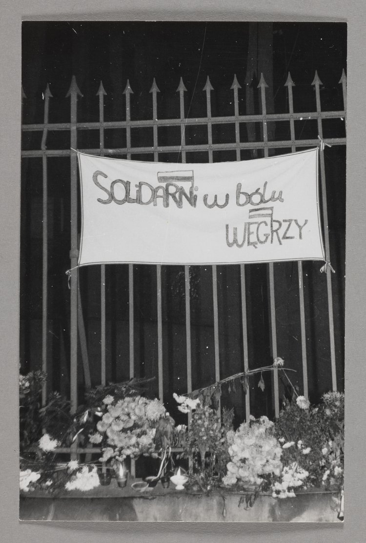 Pogrzeb bł. ks. Jerzego Popiełuszki - fragment ogrodzenia kościoła p.w. św. Stanisława Kostki na warszawskim Żoliborzu z zawieszonym transparentem oraz wiązankami kwiatów