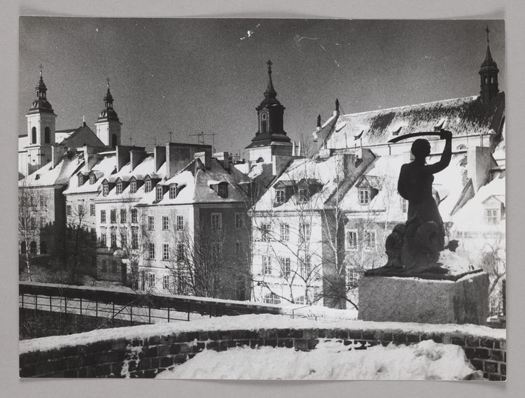 Pomnik Syreny na murach obronnych zimą; w tle kamienice przy ulicy Mostowej