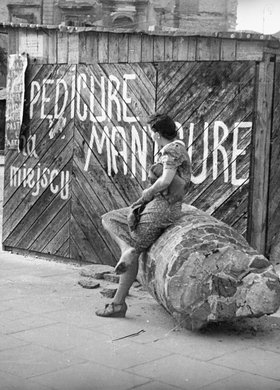 Maria Chrząszczowa siedząca na przewalonej kolumnie obok budki usługowej na Placu Trzech Krzyży