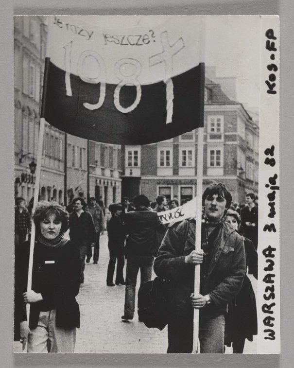 Fotografia czarnobiała ukazująca marsz członków NSZZ 'Solidarność' ulicami Warszawy w dniu 3 maja 1982 r. - maszerują oni ulicami trzymający transparenty, 3 maj 1982