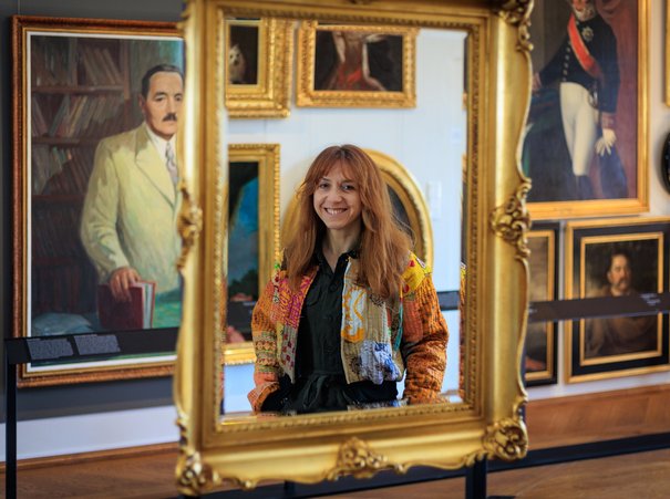 Portret Aleksandry Kresowskiej w odbiciu lustra, w tle portrety znajdujące się w Gabinecie Portretów Muzeum Warszawy