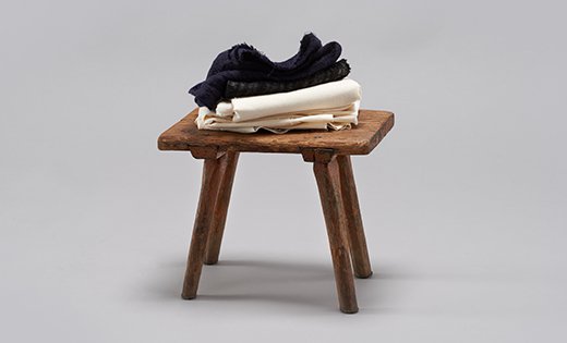 Fotografia przedstawiająca drewniany stołek, na którym złożone są dwie tkaniny - biała i czarna