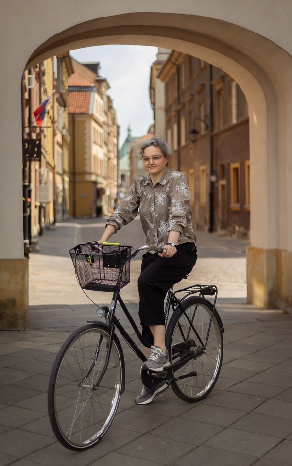 Joanna Bębenek na rowerze w tle staromiejskie budynki